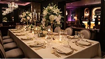 Table de banquet luxueusement dressée avec des compositions florales blanches, des bougies et de la vaisselle dorée.