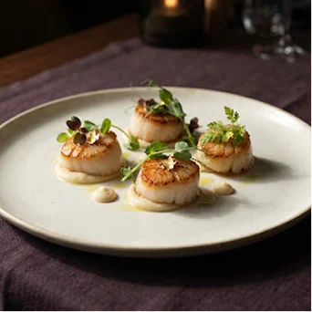 Coquilles Saint-Jacques poêlées servies sur une purée crémeuse avec des jeunes pousses et une touche de feuille d'or.